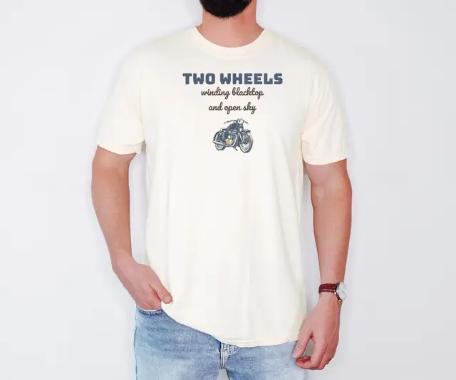 Person wearing a Ivory tee printed with TWO WHEELS, WINDING BLACKTOP AND OPEN SKY
