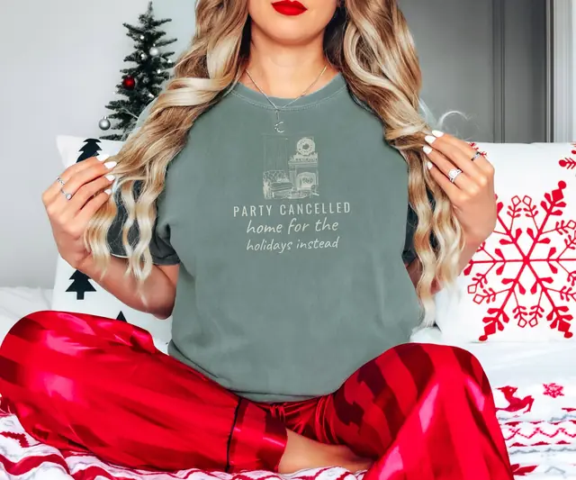 Person wearing a Moss tee printed with PARTY CANCELLED, HOME FOR THE HOLIDAYS INSTEAD