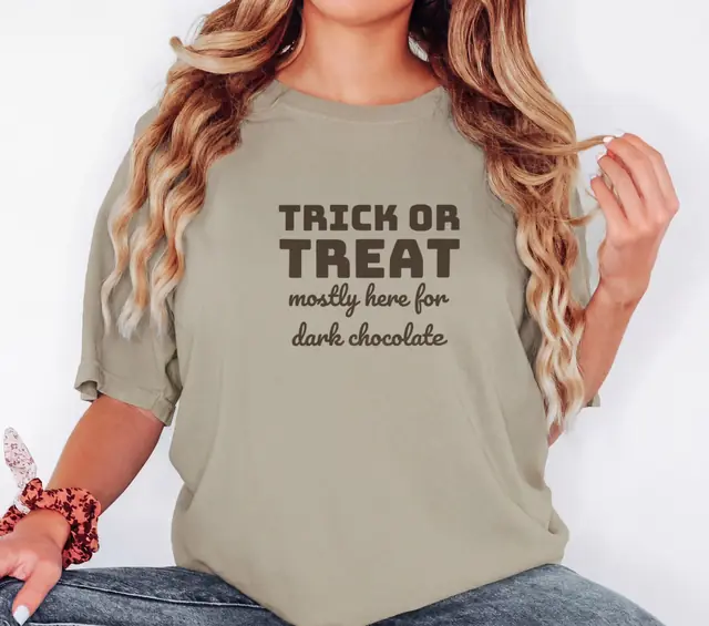 Person wearing a Khaki tee printed with TRICK OR TREAT, MOSTLY HERE FOR DARK CHOCOLATE