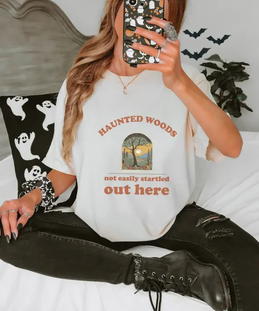 Person wearing a Ivory tee printed with HAUNTED WOODS, NOT EASILY STARTLED OUT HERE