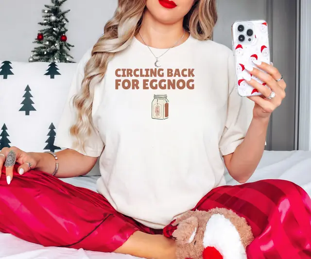 Person wearing a Ivory tee printed with CIRCLING BACK FOR EGGNOG