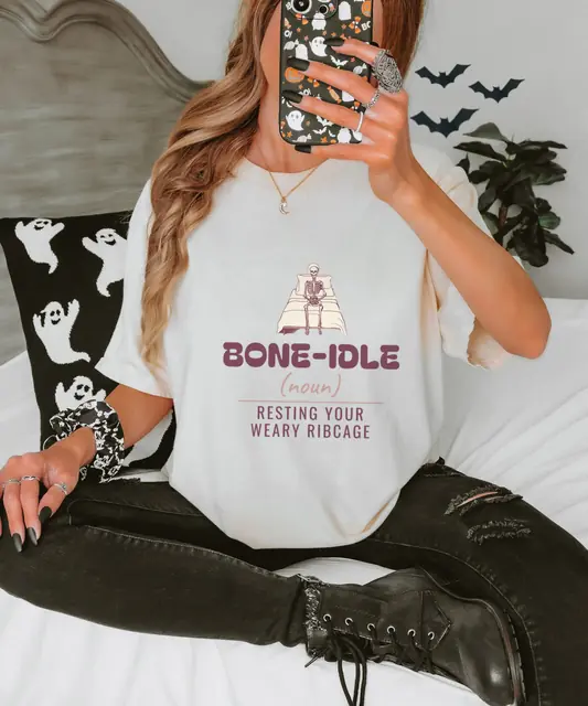 Person wearing a Ivory tee printed with BONE-IDLE, (NOUN), RESTING YOUR WEARY RIBCAGE