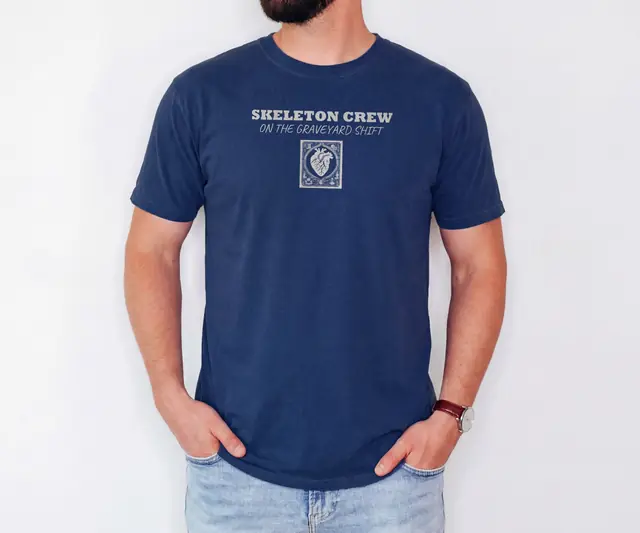 Person wearing a True Navy tee printed with SKELETON CREW, ON THE GRAVEYARD SHIFT