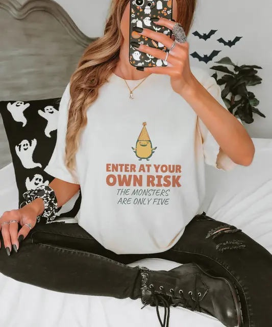 Person wearing a Ivory tee printed with ENTER AT YOUR OWN RISK, THE MONSTERS ARE ONLY FIVE