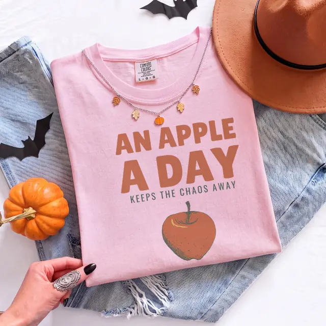 Person wearing a Blossom tee printed with AN APPLE A DAY, KEEPS THE CHAOS AWAY