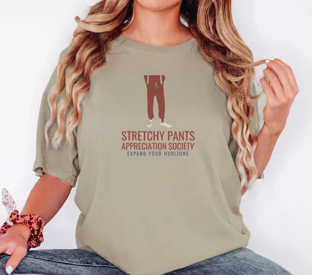Person wearing a Khaki tee printed with STRETCHY PANTS APPRECIATION SOCIETY, EXPAND YOUR HORIZONS