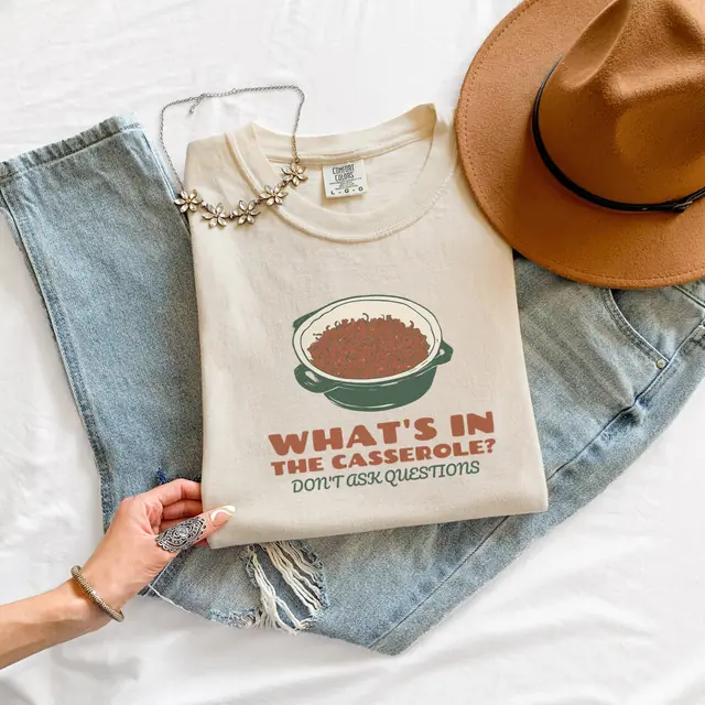 Flat-lay of a Ivory tee printed with WHAT'S IN THE CASSEROLE?, DON'T ASK QUESTIONS