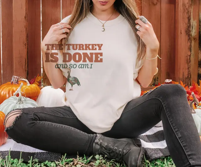 Person wearing a Ivory tee printed with THE TURKEY IS DONE, AND SO AM I