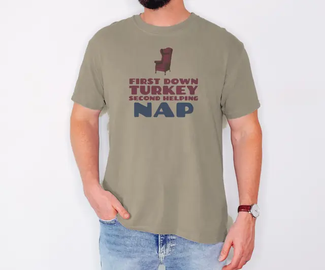 Person wearing a Khaki tee printed with FIRST DOWN, TURKEY, SECOND HELPING, NAP