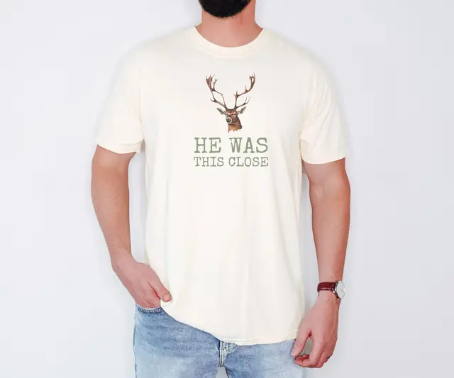 Person wearing a Ivory tee printed with HE WAS THIS CLOSE